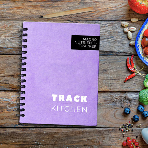 Lavender purple coil bound nutrition journal titled 'Macro Nutrients Tracker' on a wooden surface with food ingredients.