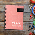 Salmon Pink coil bound nutrition journal titled 'Macro Nutrients Tracker' on a wooden surface with food ingredients.