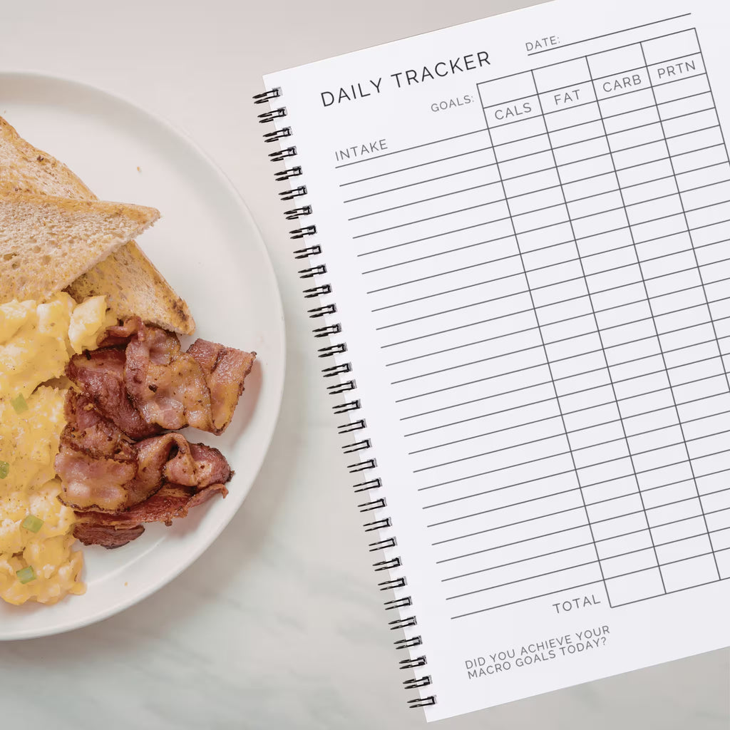 Daily Macro Nutrients Tracker journal next to a plate of breakfast toast scrambled eggs and bacon